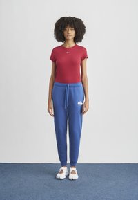 Red fitted t-shirt with short sleeves and Nike logo, paired with blue joggers featuring adjustable waistband and white Nike branding. White sneakers.