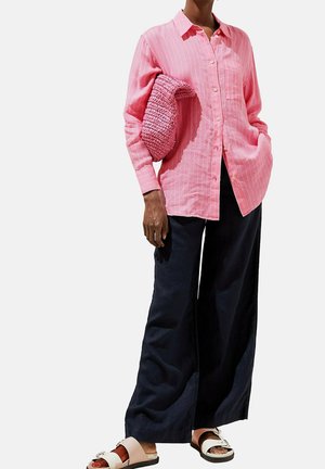 Pink striped button-up shirt with long sleeves, paired with dark wide-leg pants and patterned slip-on sandals. Holds a textured pink bag.
