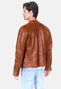 Bruine leren jas met een iets getailleerd ontwerp, voorzien van stiksels, ritssluitingen aan de mouwen en een gladde, glanzende textuur.