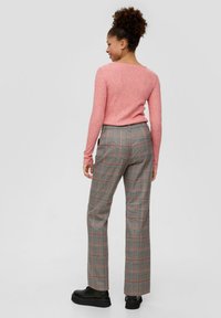 Enganliegendes rosa Rippstrickpullover kombiniert mit grauen karierten Hosen mit roten Akzenten. Model trägt schwarze Plateau-Stiefel, von hinten zu sehen.