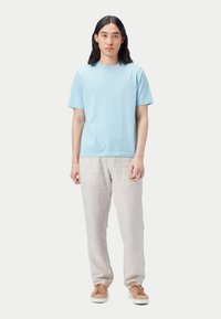 Ljusblå bomulls-T-shirt med korta ärmar, kombinerad med beige linnebyxor och bruna sneakers, stående mot en vit bakgrund.