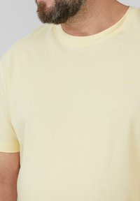 Lichtgele T-shirt met korte mouwen van zachte katoen, voorzien van een geribbelde ronde hals en een klein geborduurd logo in een contrasterende kleur.