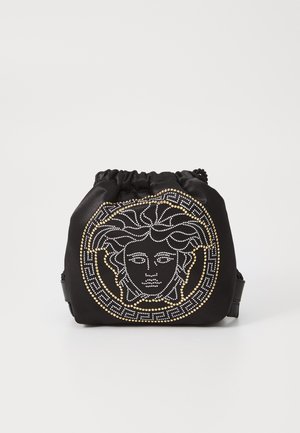 Μαύρη τσάντα drawstring από ύφασμα με κεντρικό σχέδιο πρόσωπο Μεσούσας, διακοσμημένη με λευκά και χρυσά studs, καθώς και γεωμετρικά στοιχεία.