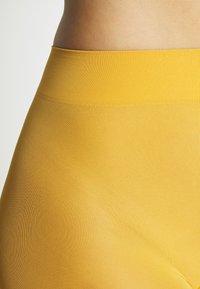 Gelbe gerippte Leggings mit hohem Bund, die eine glatte Textur und ein nahtloses Design aufweisen und einen modernen, figurbetonten Look betonen.