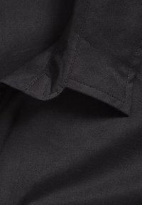 Gros plan d'un col en tissu noir avec des coutures visibles et des bords pliés sur une surface textile lisse.