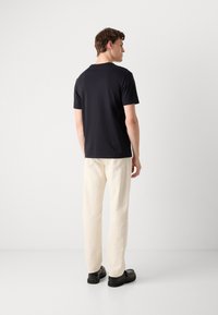 Navy short-sleeve t-shirt with a round neckline, paired with cream-colored trousers and black shoes, viewed from the back.