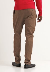 Hnědé kalhoty s texturovanou tkaninou, slim fit designem a bočními kapsami, spárované s černými botami a červeným svetrem.