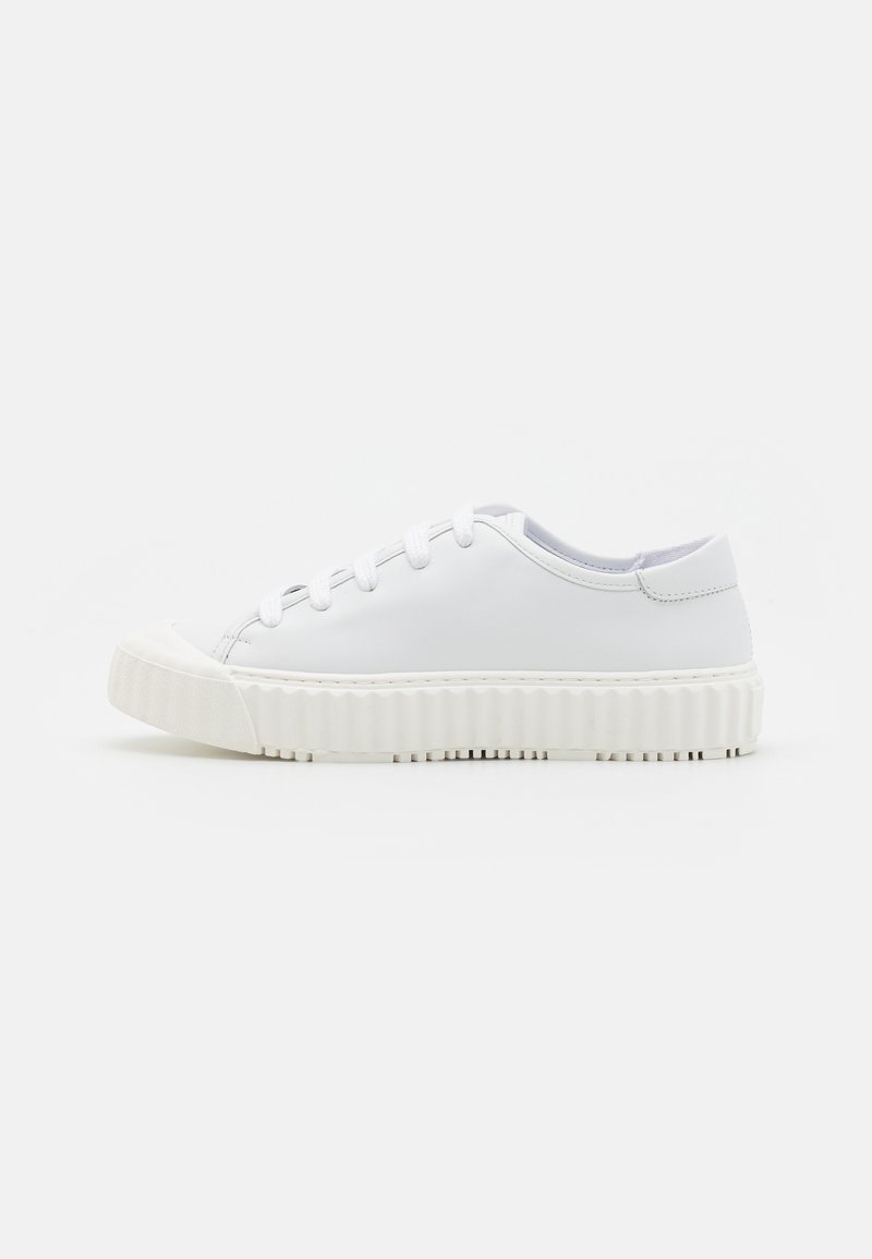 White low-top sneakers made of smooth leather with a thick, ridged rubber sole and round toe, featuring six eyelets and white laces.