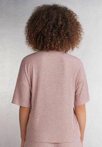 Ljusrosa ribbad t-shirt med korta ärmar, rund halsringning och en avslappnad passform, visad bakifrån. Subtil textur genom hela tyget.