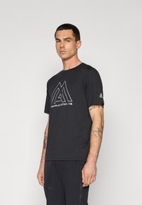 Juodas trumpomis rankovėmis marškinėlis, pagamintas iš lengvos medžiagos, su baltu geometriniu logotipu ir užrašu "MOUNTAIN ATHLETICS" priekyje.