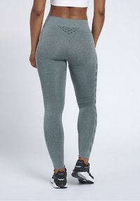 Woman wearing high-waisted grey leggings with textured detailing and black athletic shoes, standing against a plain white background.