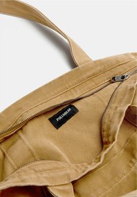 Beige színű vászontáska, cipzáras rekesszel. A belseje texturált felületű, egy fekete címkével, amin a "PULL&BEAR" felirat található.