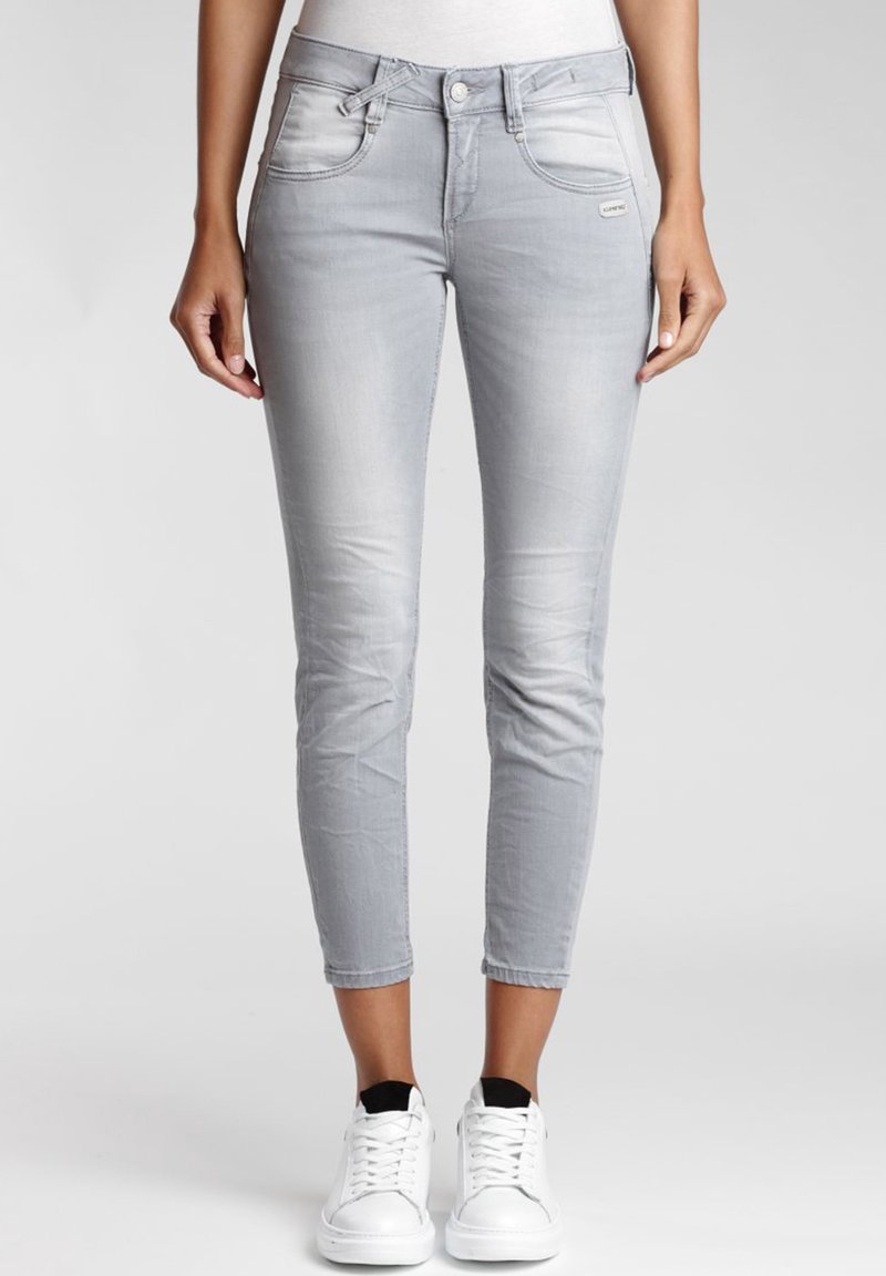Jeans skinny de mezclilla gris claro con una cintura de altura media, bolsillos frontales y detalles de desvanecimiento sutil. Combinados con zapatillas blancas.