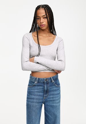 Maglietta grigia a maniche lunghe con scollo a barca e texture a coste, abbinata a jeans in denim blu a vita alta con vestibilità classica e lavaggio chiaro.