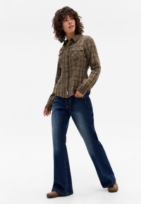 Brown plaid button-up shirt with a pointed collar and two chest pockets, paired with blue flared jeans and brown shoes.