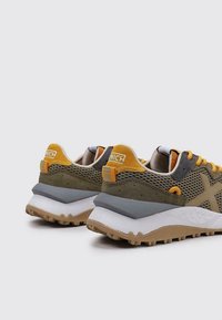 Zapatillas de malla verdes y grises con acentos amarillos, superposiciones texturizadas, una gruesa entresuela blanca y una suela de goma con patrón.