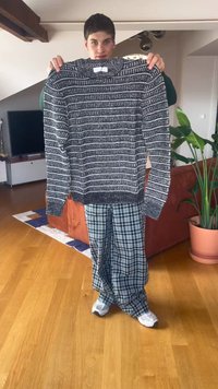 Giovane che tiene un maglione a righe bianche e nere in un soggiorno con pavimento in legno, divano arancione e pianta verde in vaso.