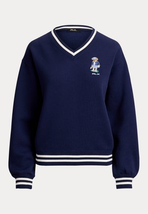Maglione blu navy con scollo a V e righe bianche su colletto, polsini e orlo, con un piccolo orso ricamato in tenuta sportiva sul petto.