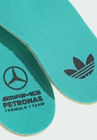 Semelles intérieures turquoise avec une surface en tissu texturé. Comportent des logos noirs : Mercedes, AMG Petronas et l'emblème à trois bandes d'Adidas.