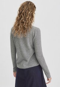 Grauer Langarmpullover aus weichem, strukturiertem Stoff; mit abgerundetem Saum und enganliegenden Ärmeln, kombiniert mit einem blauen Rock.