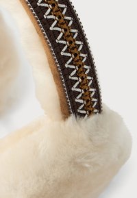 Soft cream-colored shearling earmuff with a brown and tan embroidered fabric band featuring white zigzag stitching.
