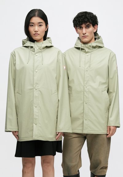 Δυο μοντέλα wearing light beige hooded rain jackets standing side by side against a plain white background.