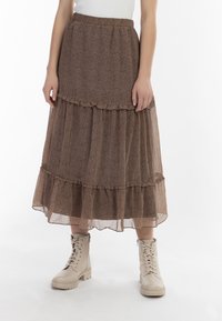 Gonna maxi marrone a strati realizzata in tessuto leggero e semi-trasparente con motivo floreale. Presenta una vita elastica e dettagli a volant sulle cuciture.