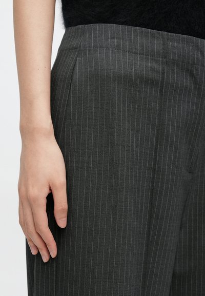 Γκρι παντελόνι με λεπτές ρίγες, ομαλή υφή, πλαϊνές τσέπες και ραμμένη εφαρμογή, εμφανιζόμενο με το χέρι να ακουμπάει στο ύφασμα.