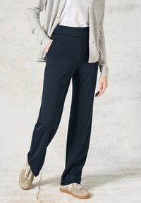 Marinemarine-brede broek van rekbaar materiaal, met een gladde textuur, hoge taille en zijzakken, gecombineerd met beige sneakers.