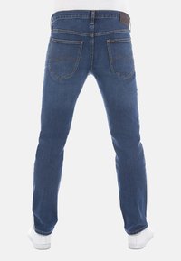 Blå denim jeans med rakt ben, med bakfickor och en brun läderetikett i midjan. Mjuk textur, medelhög midja.