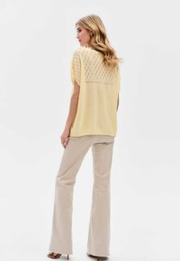 Żółty sweter z wzorem diamentowym; krótkie rękawy, luźny krój. Zestawiony z jasnobeżowymi spodniami rozszerzającymi się ku dołowi.