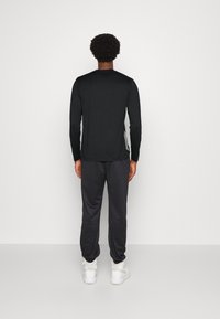 Schwarzes langärmeliges Shirt, kombiniert mit dunkelgrauen Jogginghosen. Das Outfit zeichnet sich durch einen lässigen Schnitt, eine glatte Textur und weiße Sneaker aus.