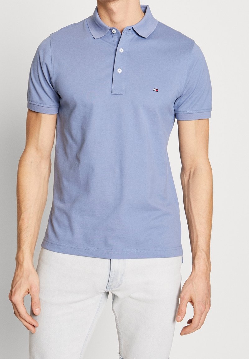 Polo bleu clair en coton, avec un col classique et une patte de boutonnage à trois boutons. Petit logo sur la poitrine, manches courtes et texture lisse.