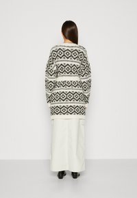 Suéter de punto en blanco y negro con patrones geométricos, de mangas largas y un corte relajado, combinado con una falda larga blanca y botas negras.