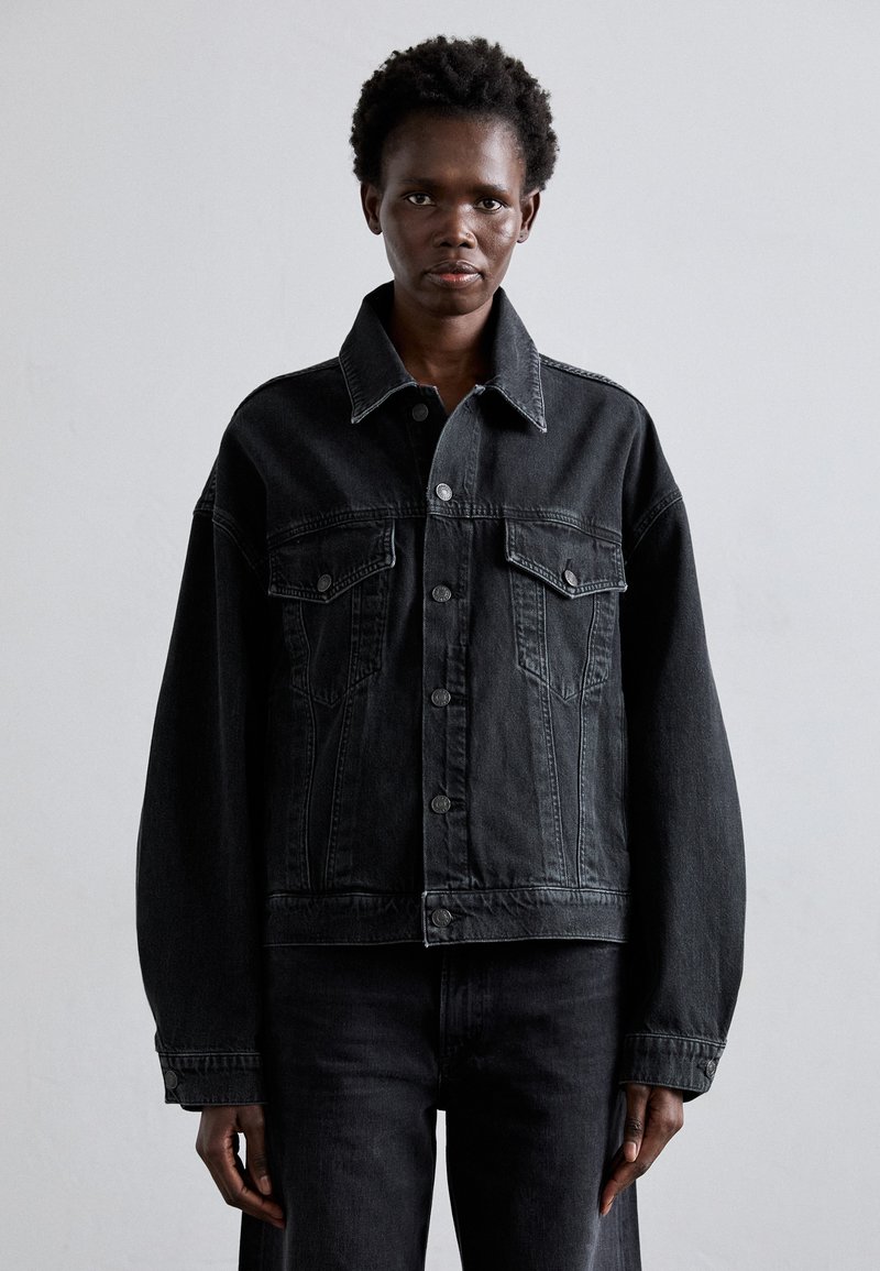 Black denim jacket with a relaxed fit, featuring two front pockets, button closure, and structured collar. Soft texture with minimal stitching details.