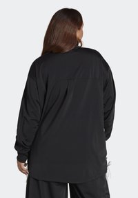 Musta pitkähihaisen paita, rento istuvuus, valmistettu sileästä kankaasta. Edessä on olkasauma ja säädettävät sivunauhat helmassa.