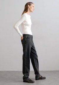 White long-sleeve top, black high-waisted jeans with side pockets, and dark shoes. Simple design, fitted top, loose pants, textured fabric.