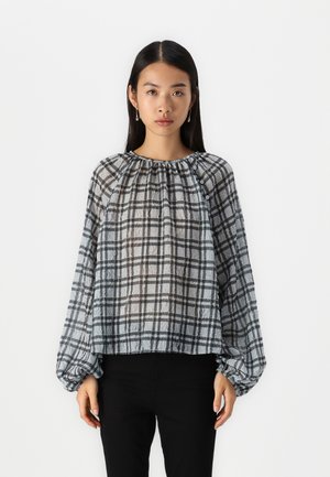 Ruudulise mustriga läbipaistvast kangast blouse, hallide ja mustade mustritega, kogutud kaelusega ja puhvvarrukatega. Kombineeritud mustade pükstega.