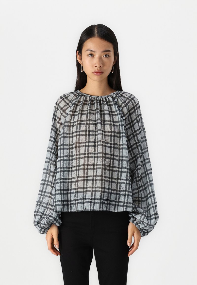 Blusa a scacchi in tessuto trasparente, con motivi grigi e neri, un collo arricciato e maniche a palloncino. Abbinate a pantaloni neri.