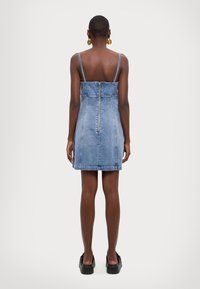 Denimkjole med tynne stropper, tettsittende liv og glidelåsdetalj bak. Lys blå farge med en myk tekstur og rett nederkant.