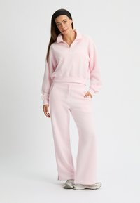 Roze fleece quarter-zip pullover met geribbelde manchetten, gecombineerd met bijpassende wijde broek. Bevat een logo op de borst en zijzakken.