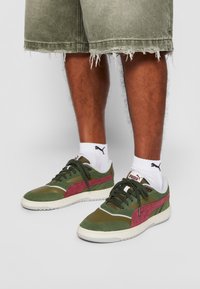 Men's green and burgundy sneakers with a mixed material design, featuring laces, a white sole, and contrasting accents on the sides.