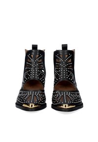 Botines negros con diseño recortado, acentos metálicos y tachuelas plateadas. Textura de cuero suave con puntera redondeada y lados abiertos.