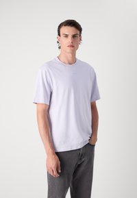 T-shirt à manches courtes en lavande, col rond, en tissu doux, coupe décontractée. Associé à un jean gris foncé, avec un détail de logo minimaliste sur la poitrine.