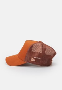 Gorra naranja con una parte delantera sólida y parte trasera de malla. Visera redondeada y cierre de presión ajustable. Presenta un logo en el lado.