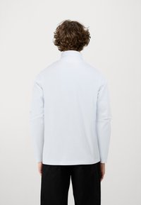 Hosszú ujjú, világoskék ing, magas gallérral és sima textúrával, fekete nadrággal párosítva. Minimalista dizájn, látható minták nélkül.