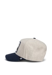 Gorra con un cuerpo de lino crema y visera de mezclilla azul oscura. Presenta un parche en la parte frontal con detalles bordados. Diseño estructurado de seis paneles.