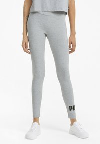 Leggings grises de tela elástica, con un diseño ajustado y un acento de logo en la parte inferior, combinados con zapatillas blancas.