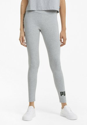 Leggings grises de tela elástica, con un diseño ajustado y un acento de logo en la parte inferior, combinados con zapatillas blancas.