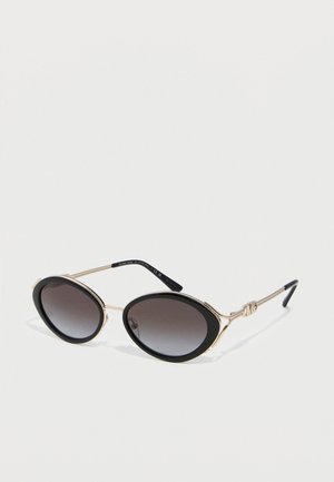 Oval black sunglasses with gold metal frames and gradient dark lenses placed on a white surface.
